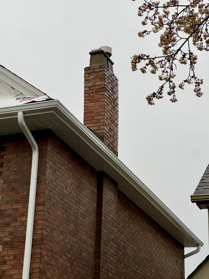 Deteriorating brown brick chimney with a cracked concrete crown and spalling brick before rebuild, Toronto home