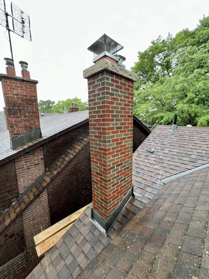 Rebuilt red brick chimney with a new stone crown and mesh cap on a Toronto shingle roof