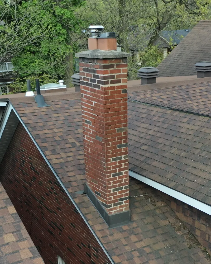 Cracked red brick chimney with a corroded metal cap before rebuild, Toronto shingle roof
