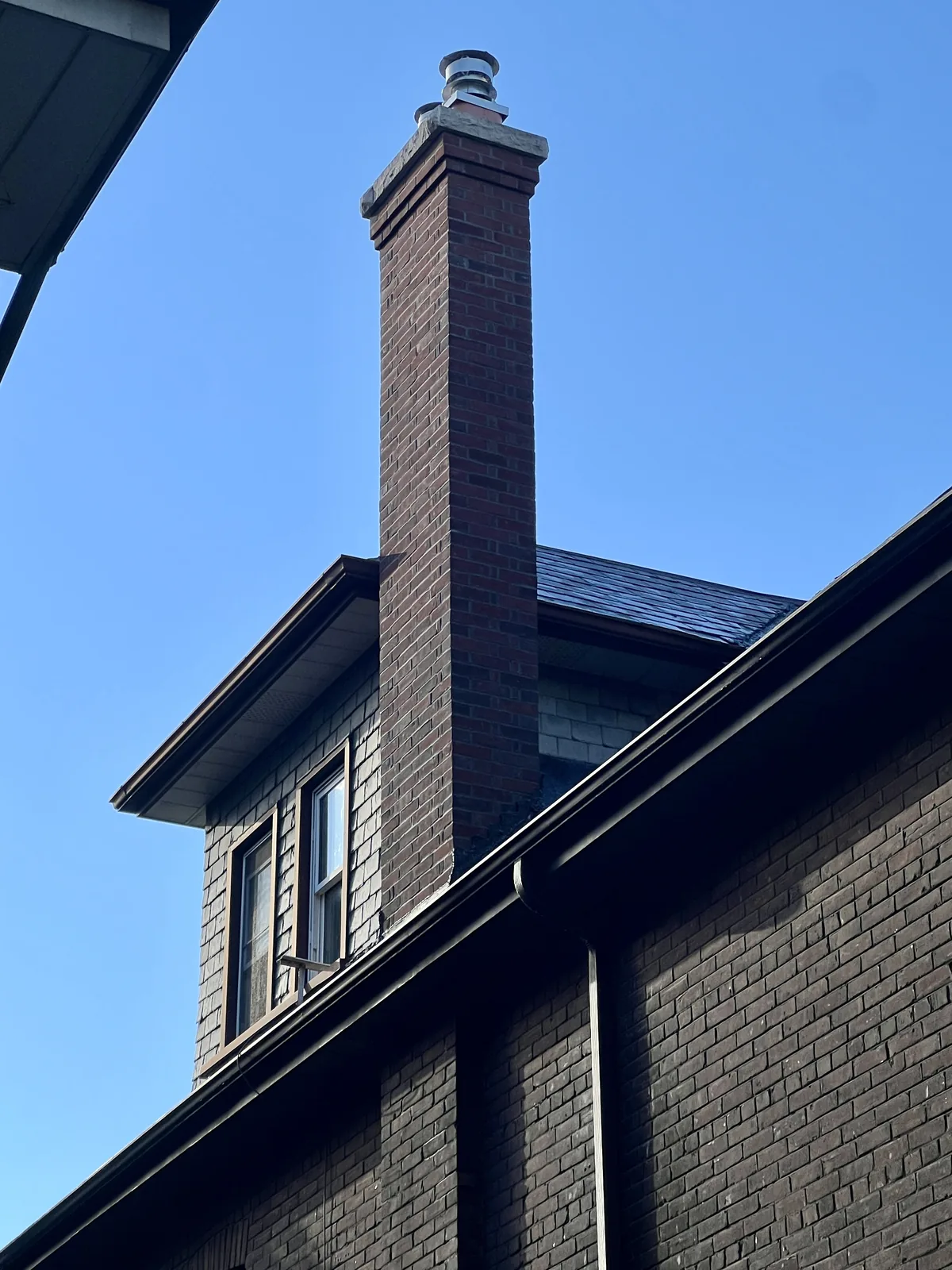 Slender red brick chimney rebuilt to code with a corbelled cap and cast stone crown above a slate roof, Toronto