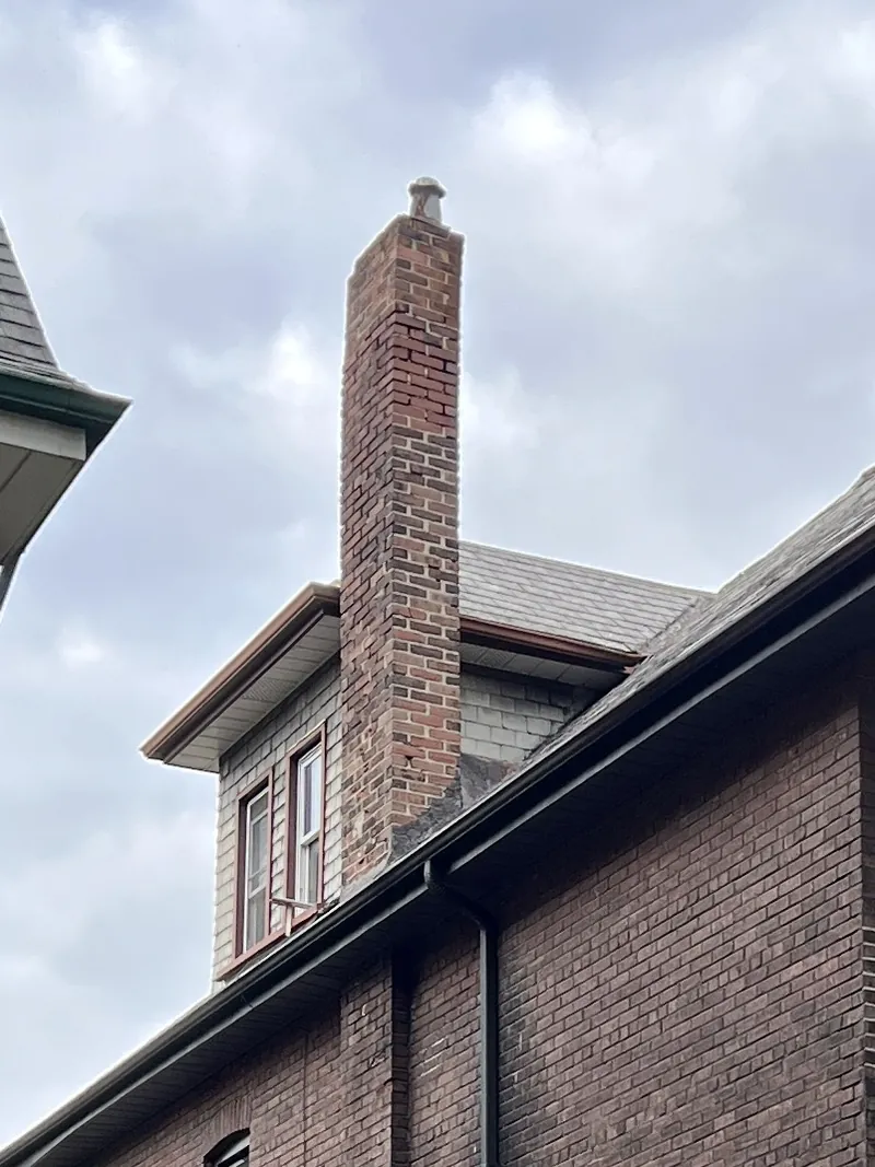 Old spalling red brick chimney with eroded mortar above a slate roof before rebuild, Toronto