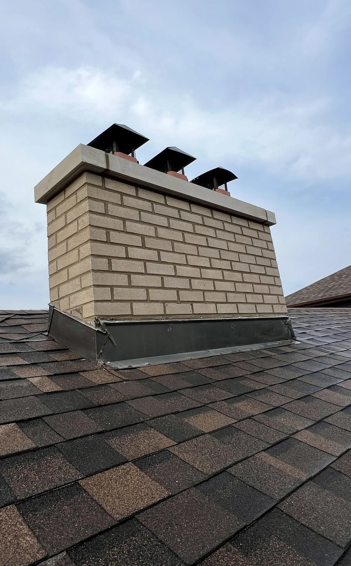 Rebuilt buff brick three-flue chimney with a cast stone crown and new caps, Toronto